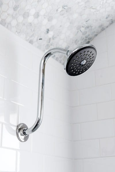 Hand-honed marble hexagonal tile in arched shower ceiling with showerhead.