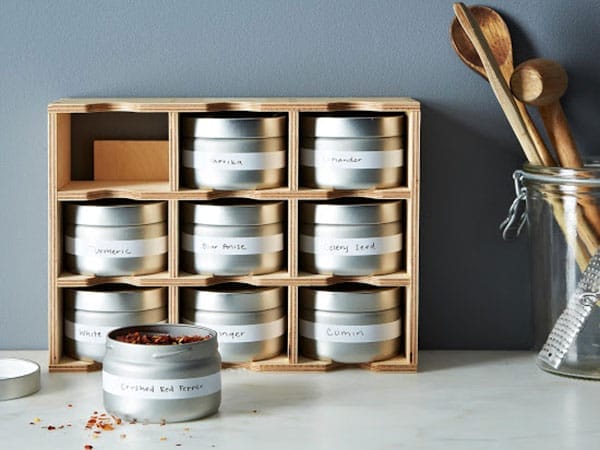 Three-level wooden spice rack holding silver jars of spices.