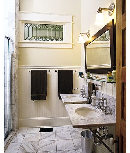 Elegant pre-war bathroom with Carrara marble countertops, nickel-plated fixtures, glass shelving, and stained oak woodwork mirror.