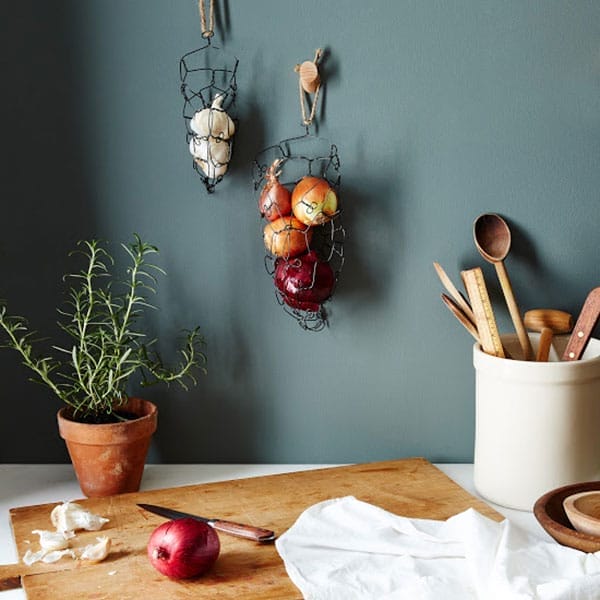 Two wall-mounted black wire baskets holding onions and garlic.