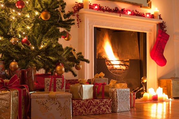 a lit fireplace with candles surrounding it and packages under a Christmas tree