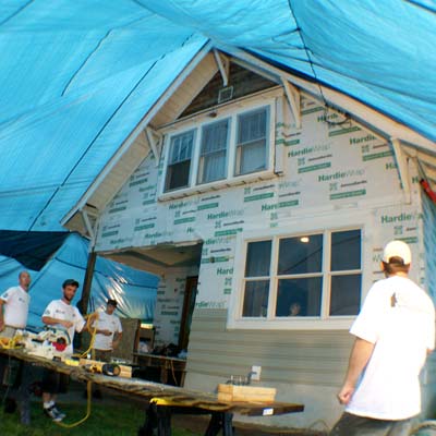 Workers standing by a house under a tarp.