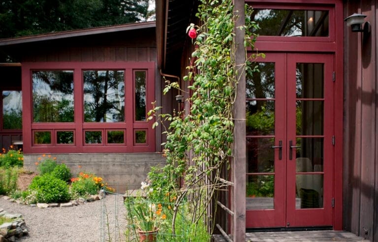 House with brick red window frames surrounded by climbing vines on neutral walls.