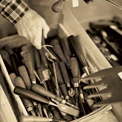 A person reaches into a box of chisels and gouges, two common antique tools.