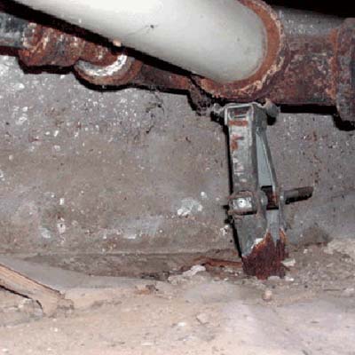 Rusted car jack supporting cast iron plumbing in crawl space.