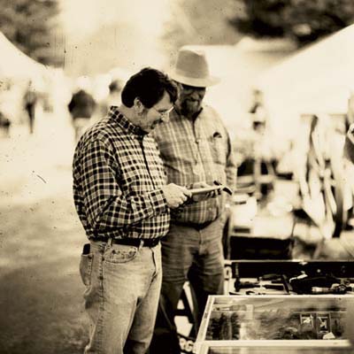 Norm Abram and another person look at an antique hammer in a market.