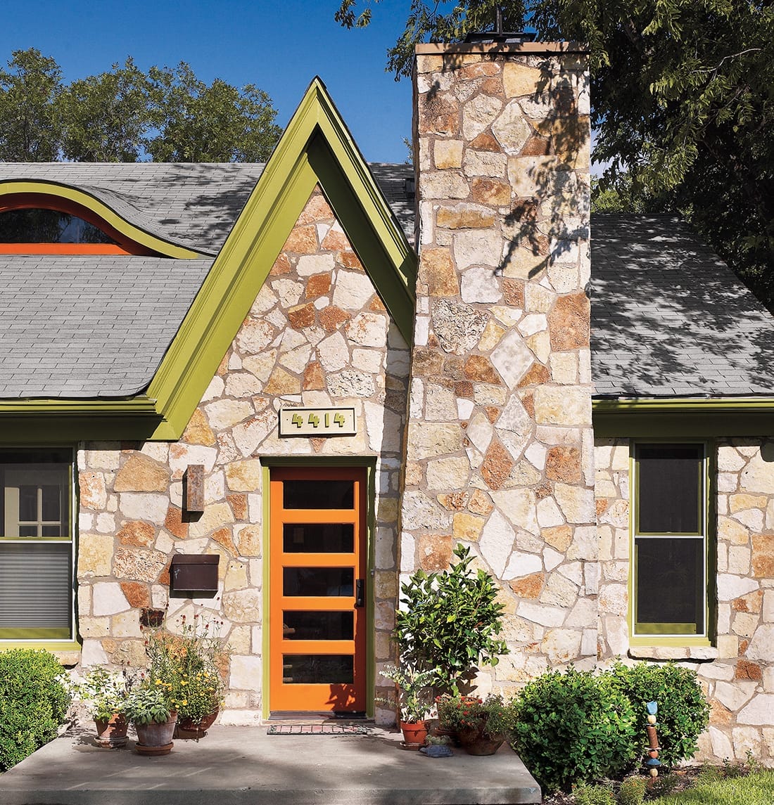 A charming house with a stone exterior features a modern orange fiberglass entry door framed by green trim.