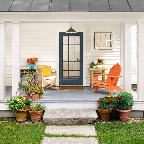 Two chairs and plants on a front porch.