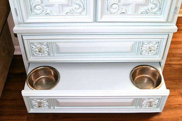 A dog food station with two bowls in the bottom drawer of a white dresser.
