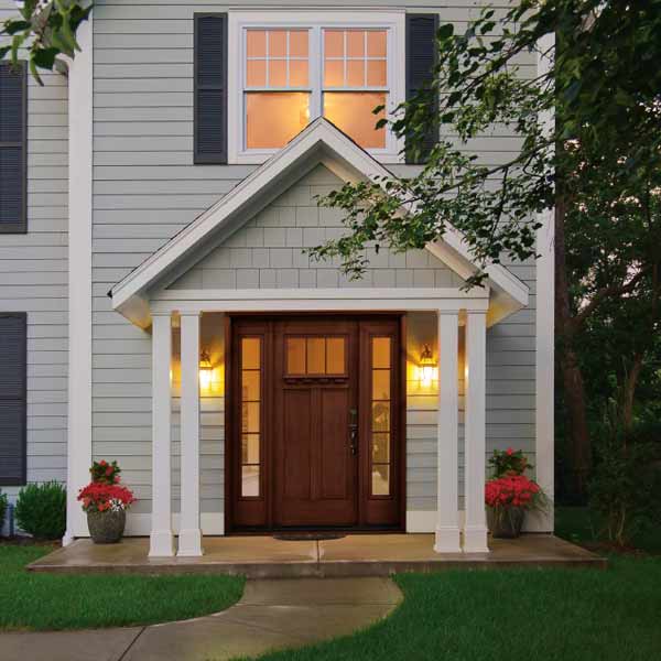 A brown fiberglass entry door flanked by sidelights and with a small covered porch on the front of house with gray siding.