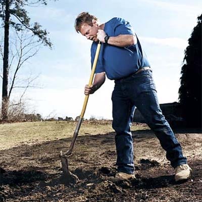 A man chops up dirt with his shovel before digging.