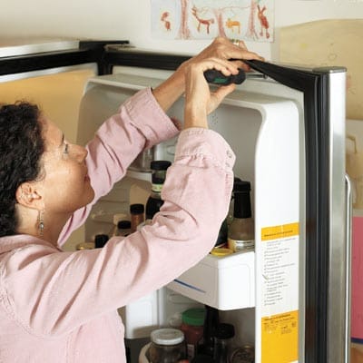 Homeowner installing a replacement refrigerator gasket.