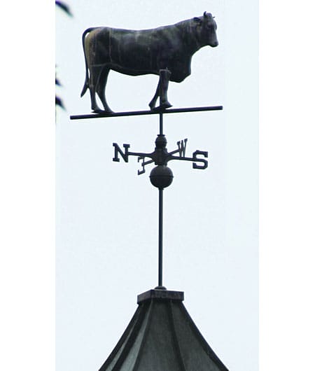 A  black metal weathervane with a cow on top.