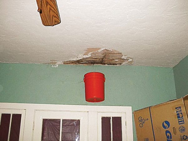 Bucket hanging from wall to catch water from leaking roof.