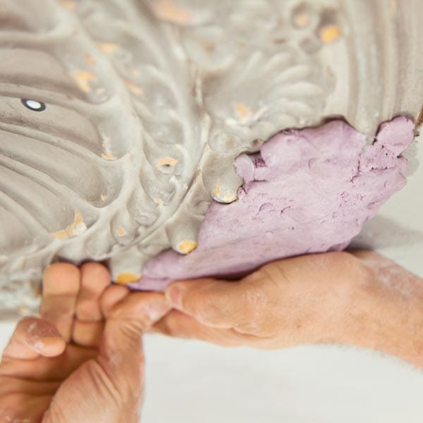 Two-part modeling putty being pressed onto undamaged medallion section to create flexible mold for replication.
