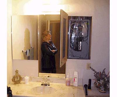 Main electrical panel hidden behind bathroom mirror violating safety codes.