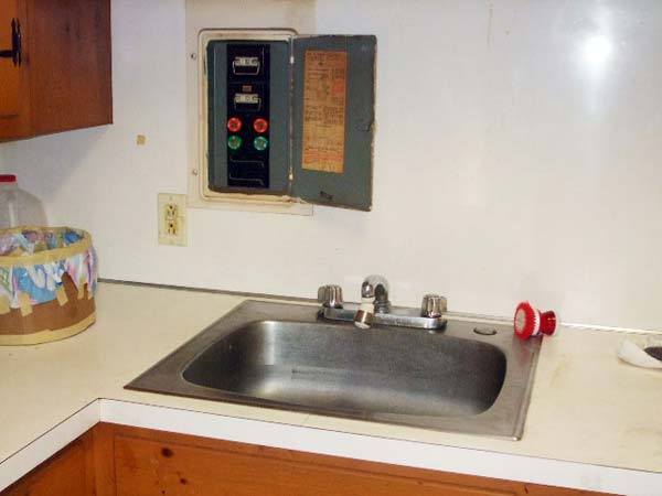 Live electrical fuse box installed dangerously close to kitchen sink.