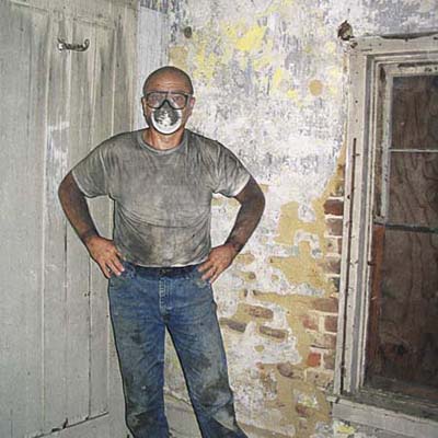 A man in a dust mask stands in an old kitchen