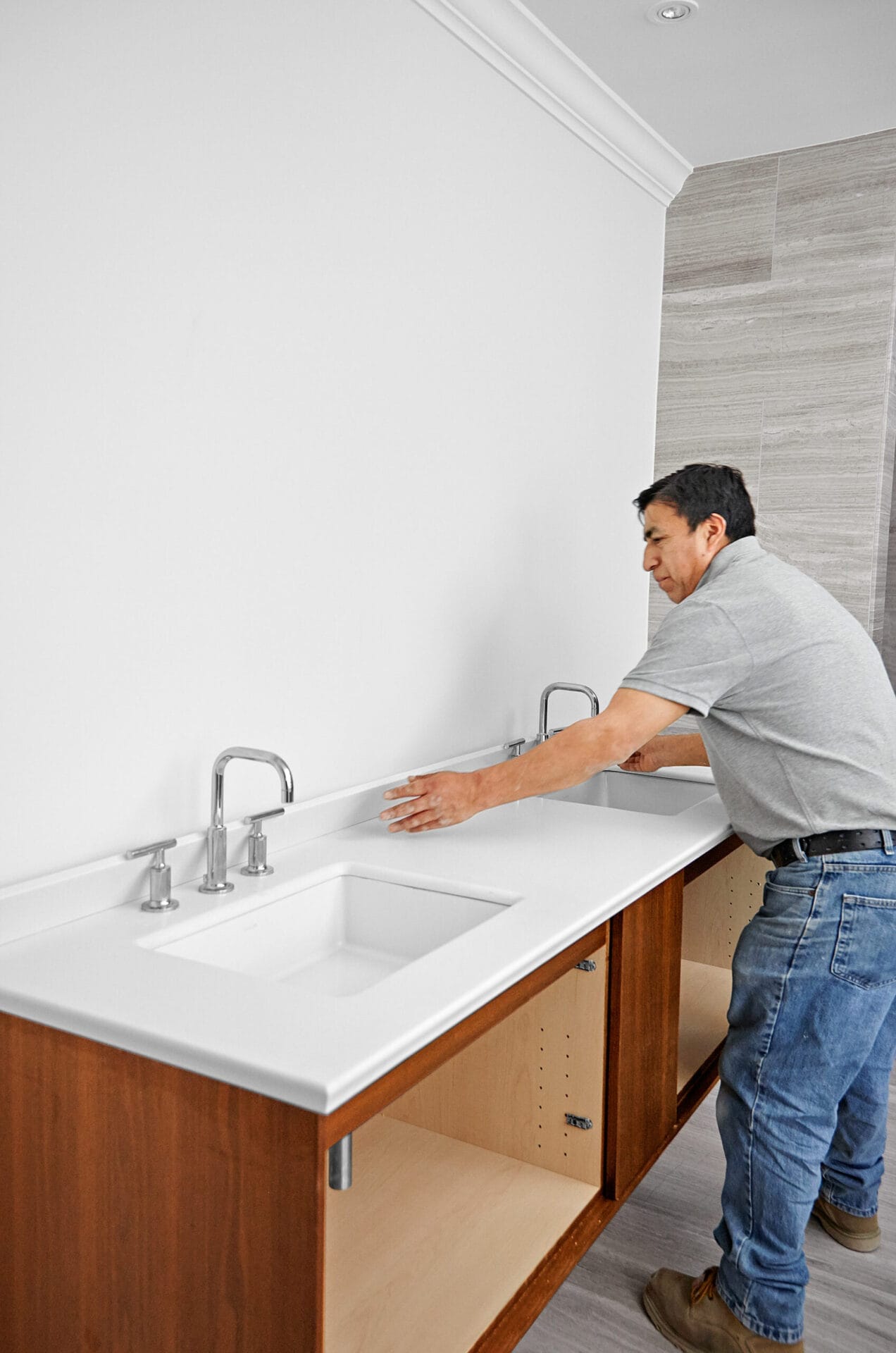 A man adds backsplash to the wall-mount vanity and sink.