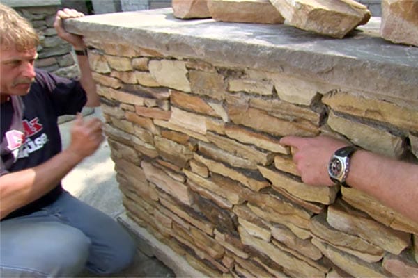 Man kneeling next to stone wall.