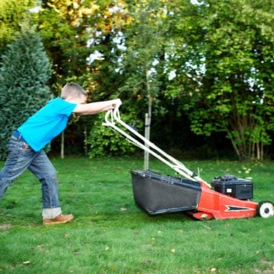 Young boy pushing a lawn mower.