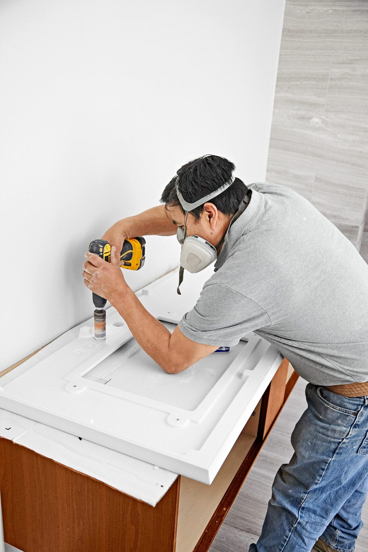 A man drills in wall-mount vanity for sink faucet.