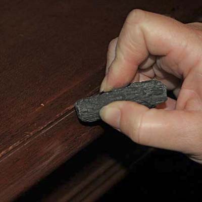 charcoal being used to fix a scratch on a piece of wood furniture
