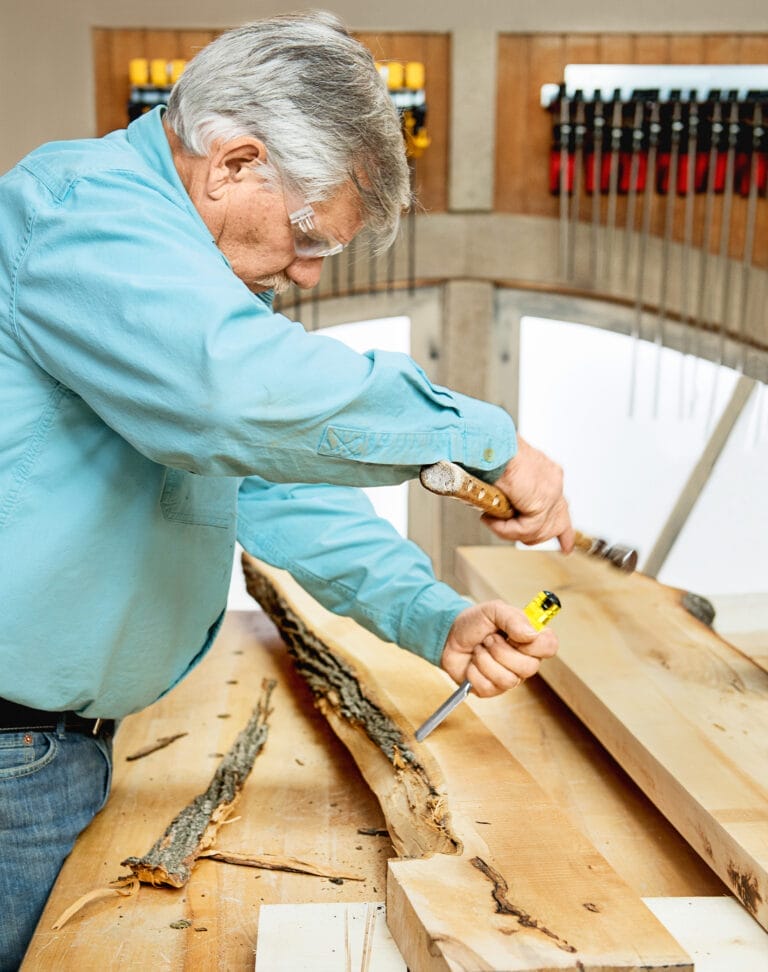 Tom Silva removes the bark from a wood slab with a chisel so it can be used for a table.