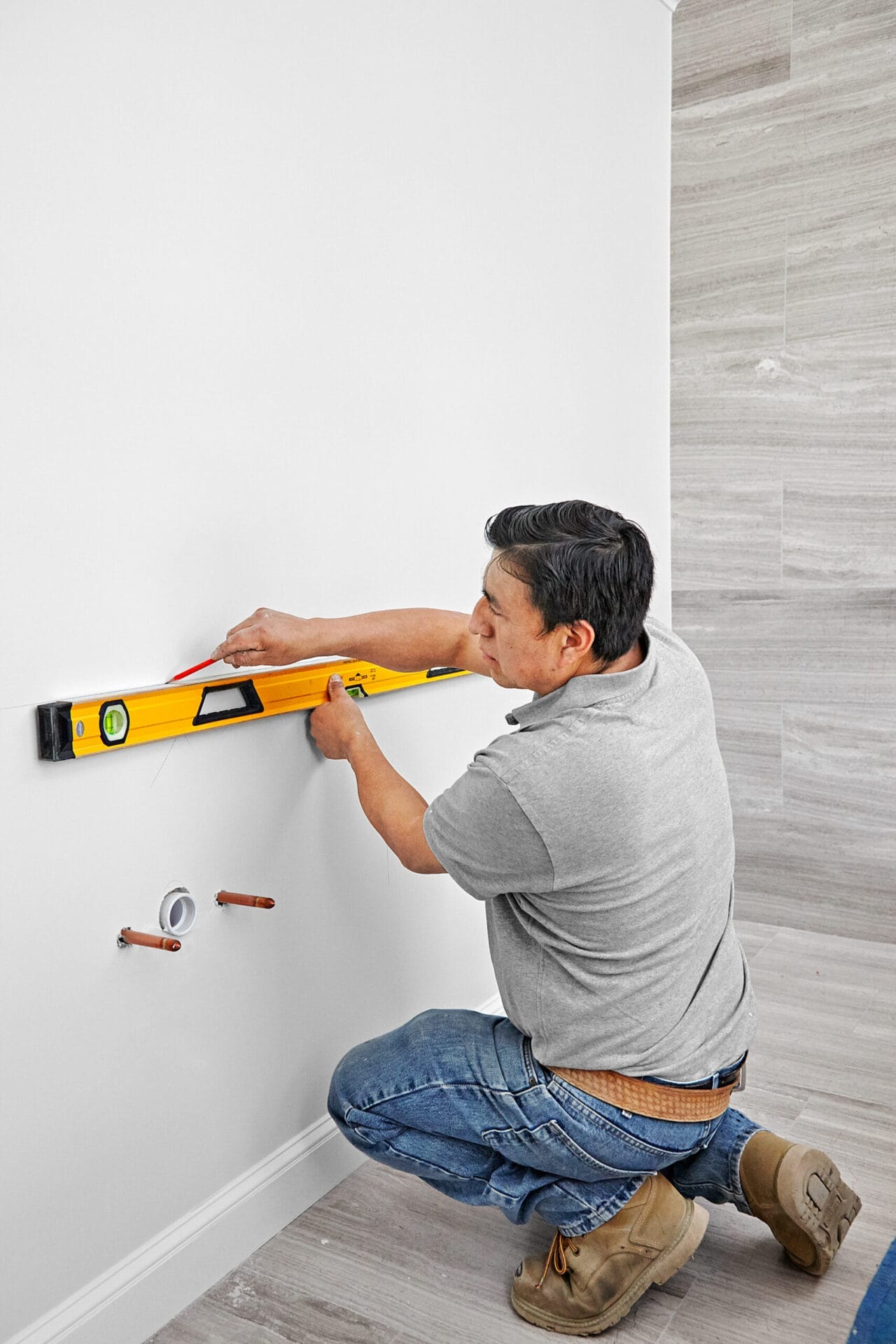 A man uses a level to mark on the wall for the wall-mount vanity and sink.