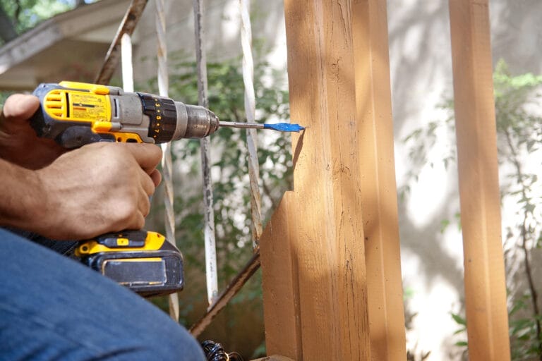 A man using a drill to put a hole in a deck.