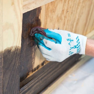 A person applies wood stain to the lily pond box.