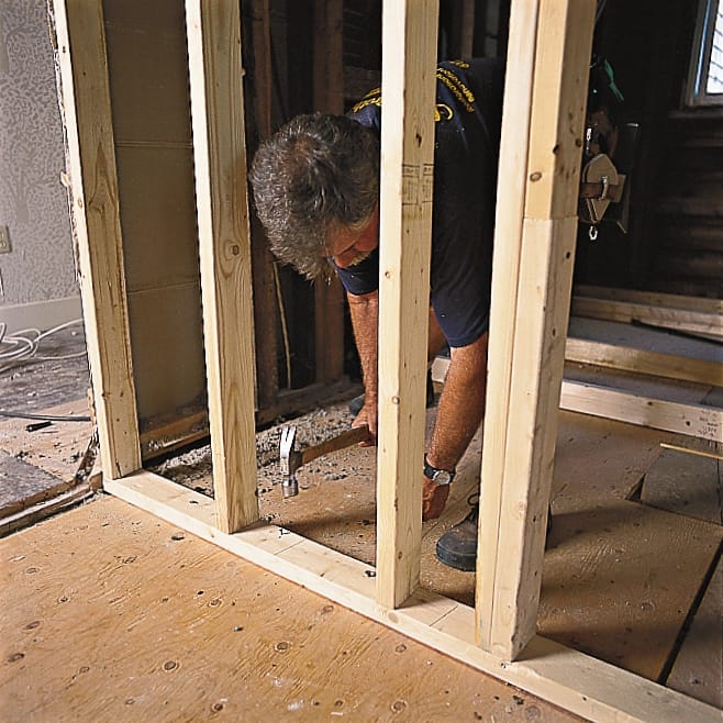 A builder nails the partition wall frame into the preexisting structure of the house.