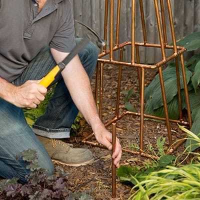 Person tapping copper leg stakes into garden soil.