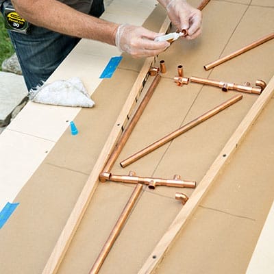 Hands applying super glue to copper tee fitting joint.