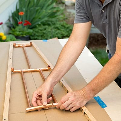 Hands connecting copper uprights between assembled rung tiers.
