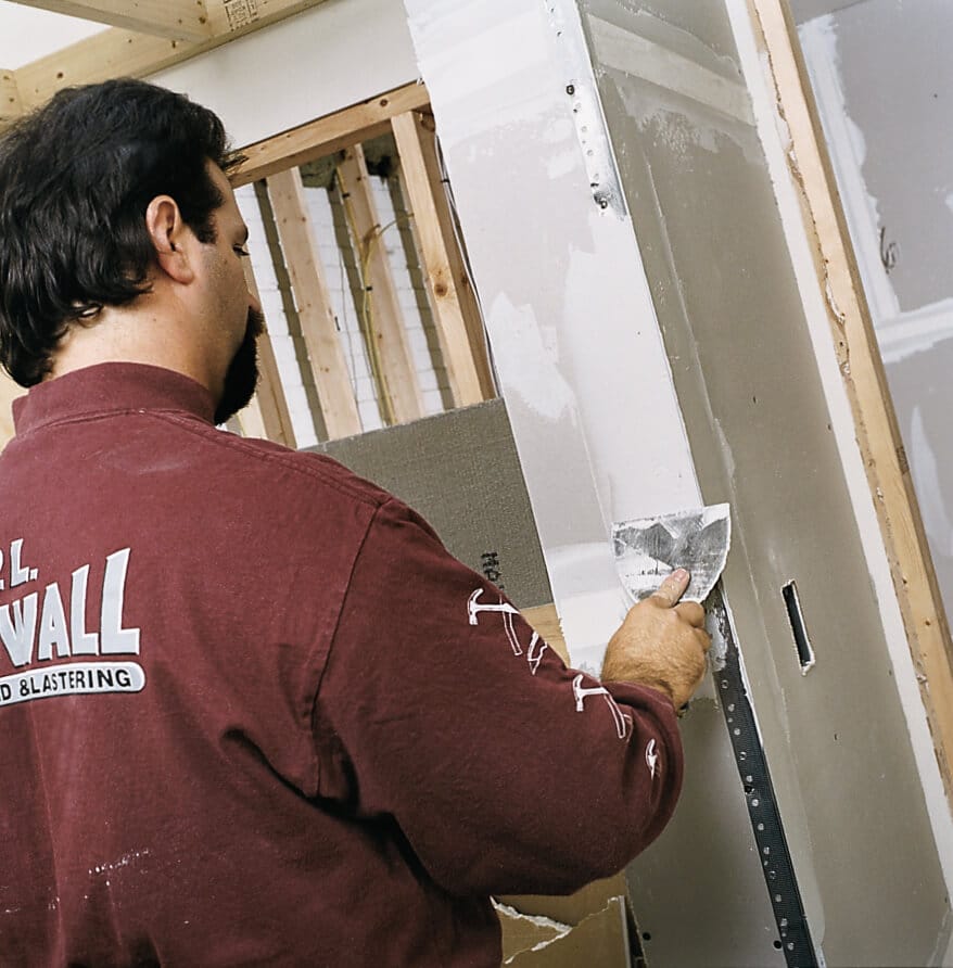 A man finishes drywall cornerbeads by using a drywall knife to cover the corner with a compound.