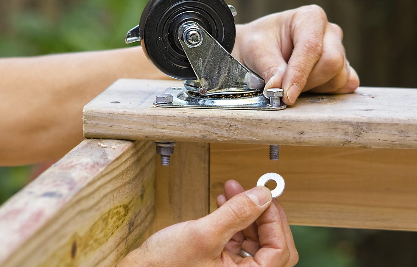A person attaches casters to the base plates on the frame of a privacy planter.