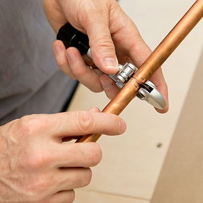 Tube cutter tool cutting copper tubing at marked line.