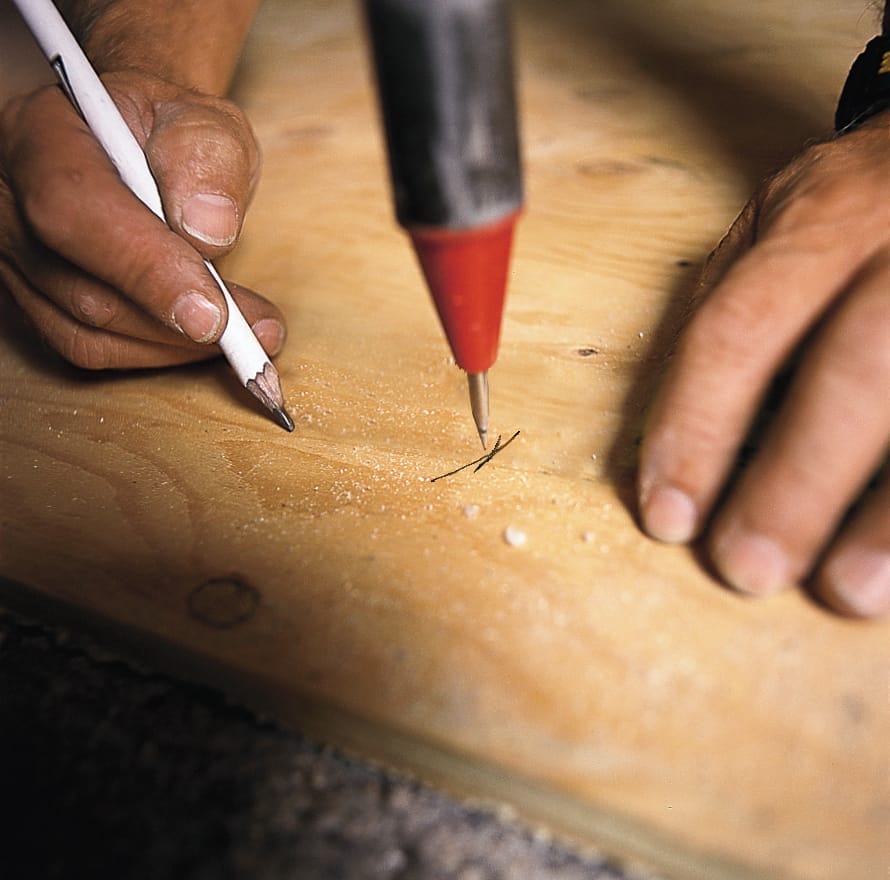 A builder uses a plumb bob to make sure that marks on the floor and ceiling of the partition wall framing are aligned.