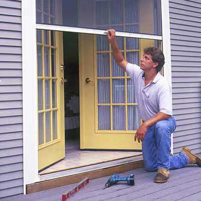 A man works on tension adjustment of his retractable screen door.