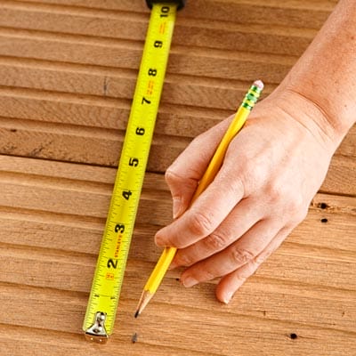 A person measures and marks wood to be a coffee table shelf.