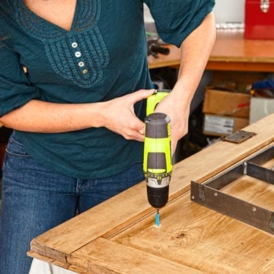 A woman drills pilot holes into the salvaged cabinet door for the legs.