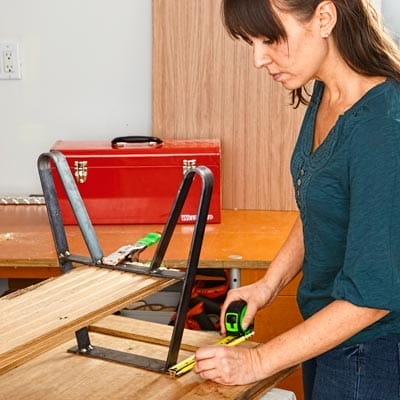 A woman measures where to put legs for a coffee table on a salvaged cabinet door.