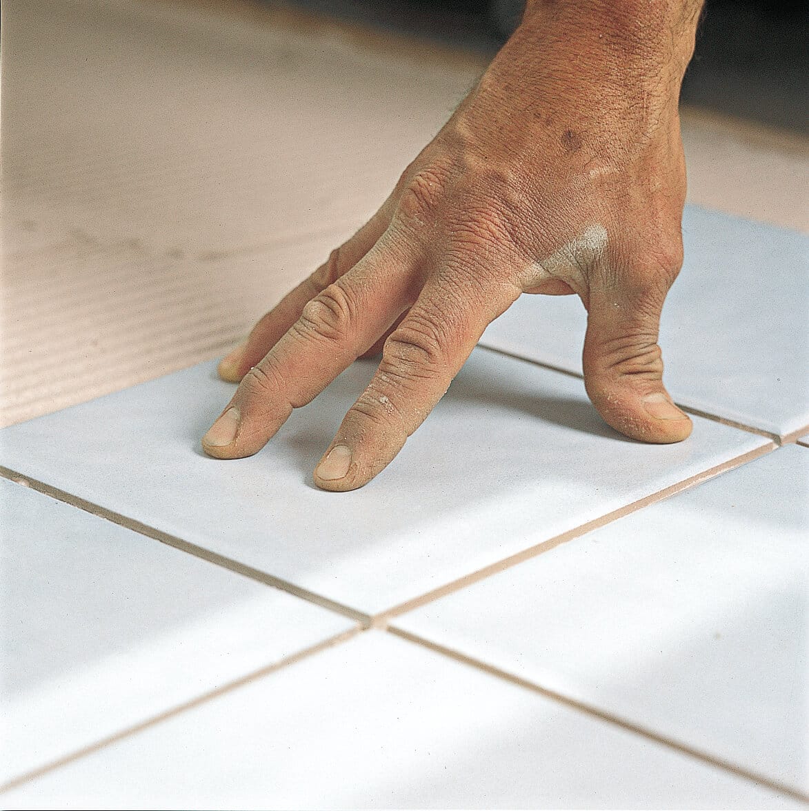 A man setting tile into place on a bathroom floor.