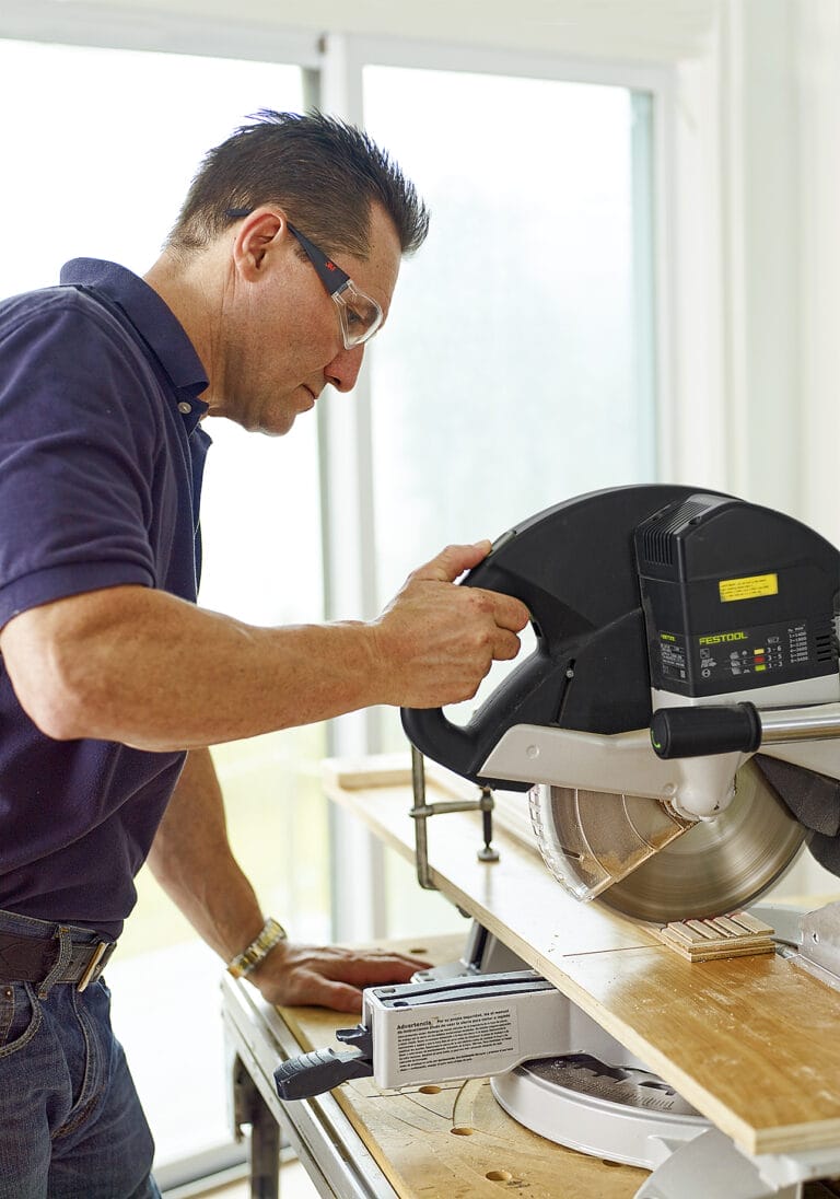 A man uses a miter saw to cut floor planks to the right length for the herringbone floor.