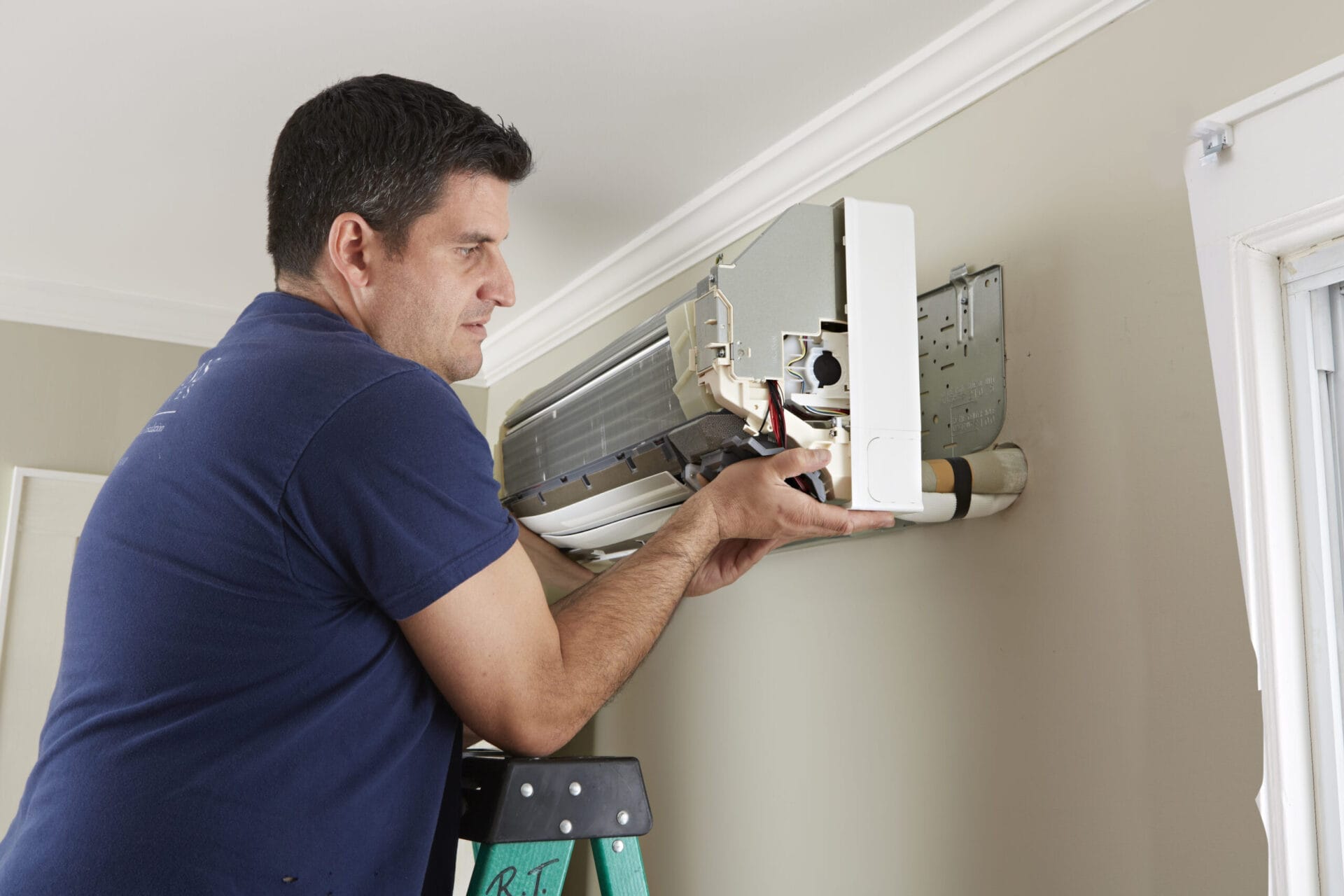 A man mounting an air handler on the wall of a house.