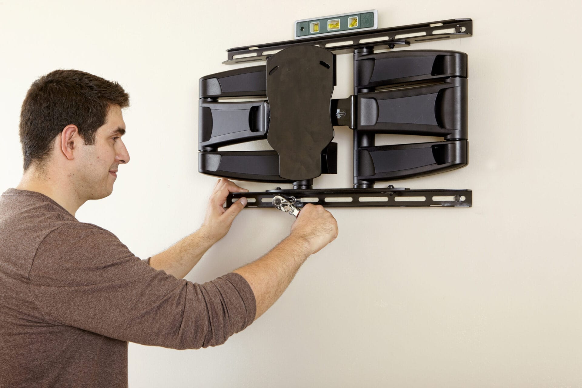 A person uses a wrench to secure a TV wall mount to the wall, with a level placed on top to ensure proper alignment.