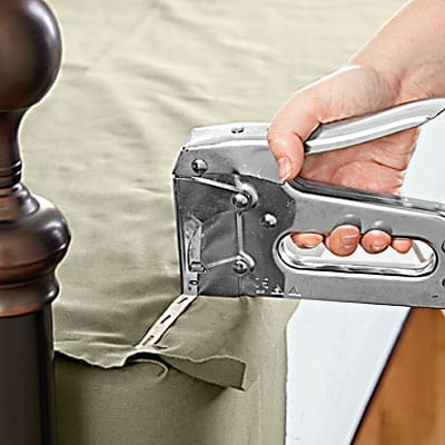A man using a device to affix the side of a box spring cover.