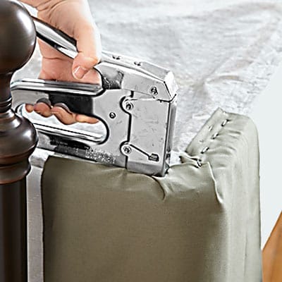 A man using a device to affix the corner of a box spring cover.