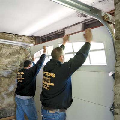 Two men add the last section of a carriage style garage door.